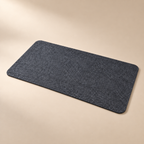 The Felt Desk Mat in charcoal wool felt, lying flat on an oat background